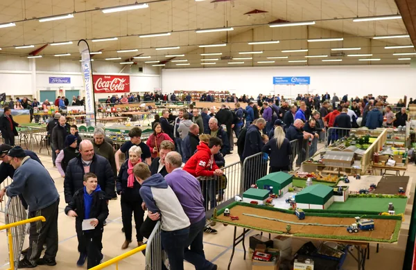 A crowd filling the boarded floor at a model fair, around stalls and display tables