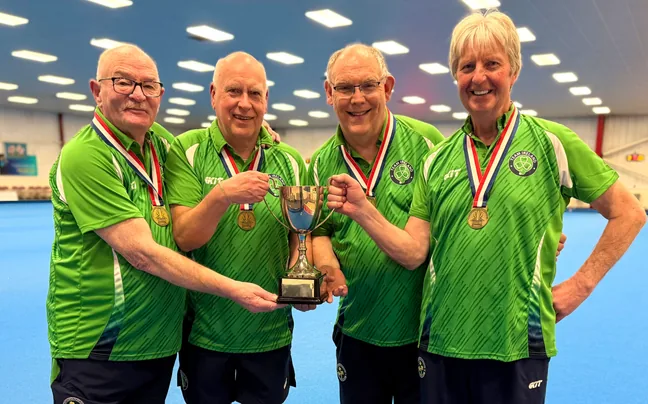Four County Antrim bowlers in green shirts holding a trophy on the green